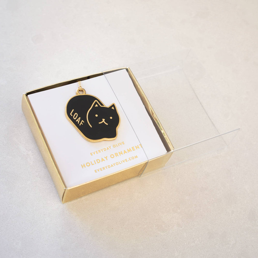 Black cat-shaped ornament with 'LOAF' on a gold card in a box on a light gray background