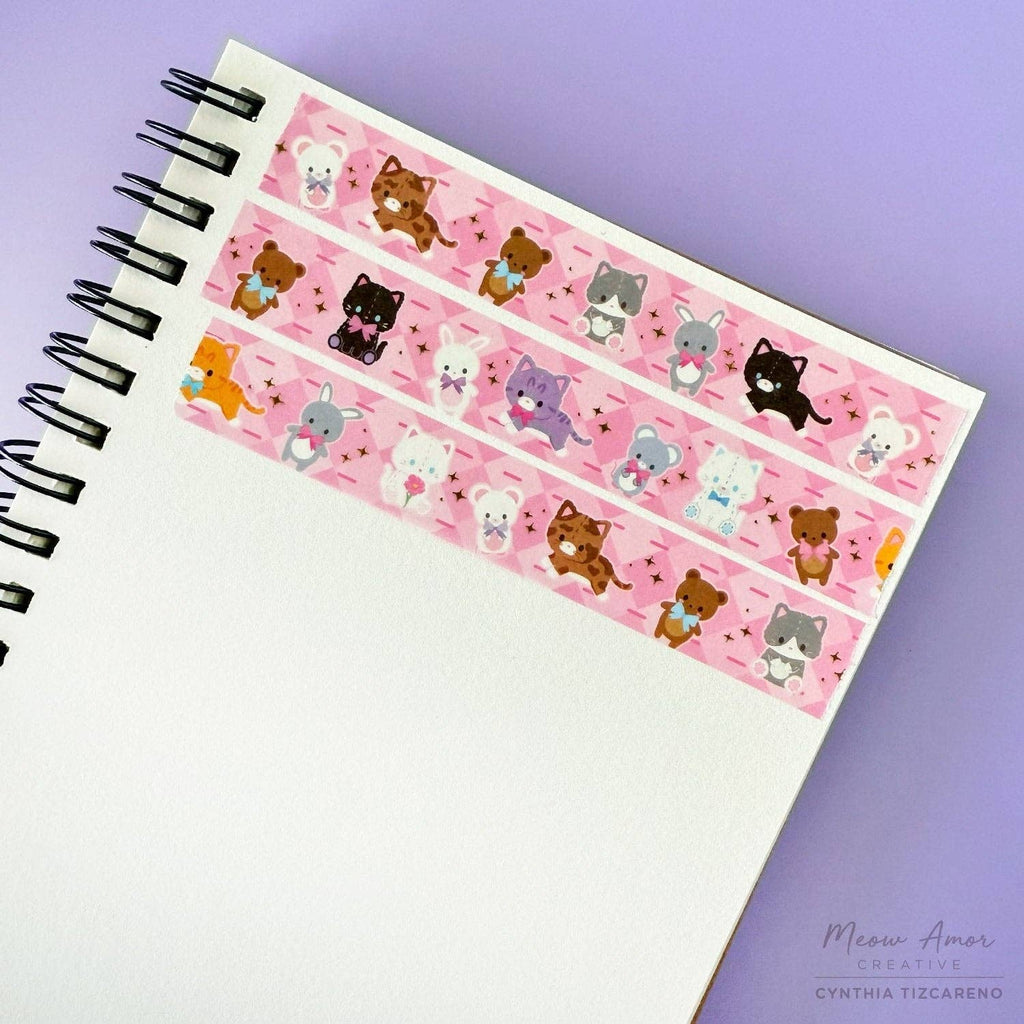 Notebook with decorative washi tape featuring cats that look like plushies on a pink background.