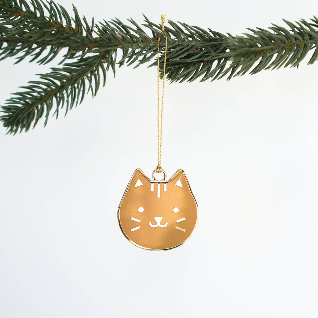 Gold cat-shaped ornament hanging from a branch on a white background