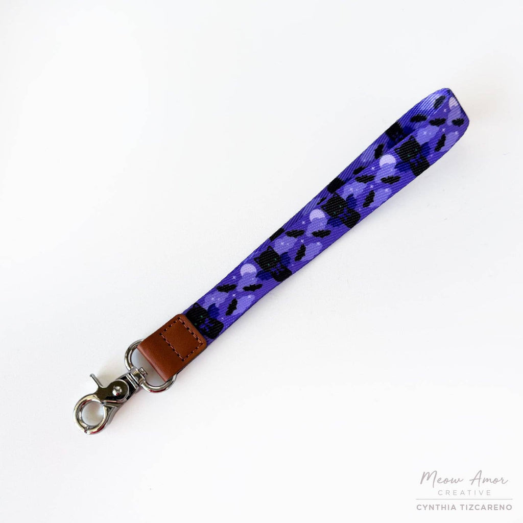 Purple lanyard with black cat pattern and brown leather strap on a white background